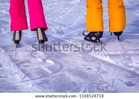 Legs of teenagers girls, boys in bright pink yellow clothes in ice skates, closeup skating shoes in winter, healthy lifestyle.