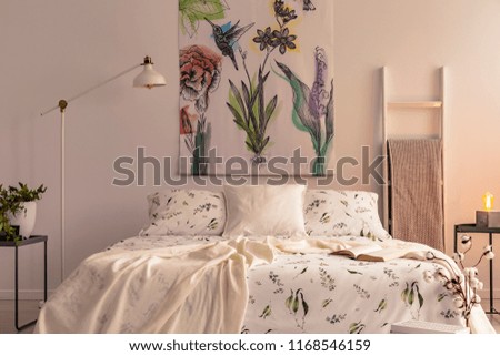 Flowers and a hummingbird painted on the fabric above a bed which is dressed in green plants pattern light color bedding in a cozy bedroom interior. Real photo.