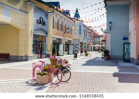 Europe street paper lanterns shops day Sunny, vintage pink Bicycle stands outside street shops, large glass storefronts, cobblestone floor