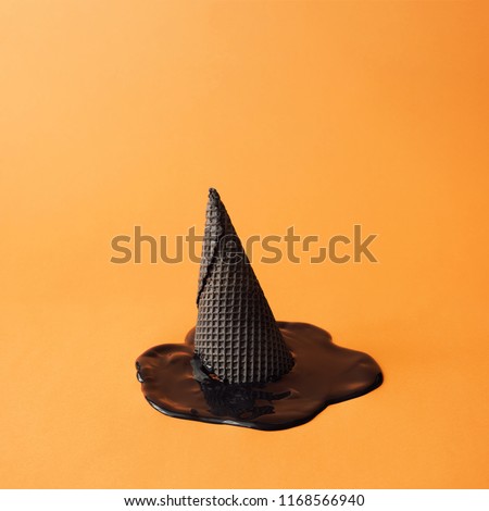 Witch hat made of black ice cream cone with melted black ice cream on orange background. Halloween minimal concept.
