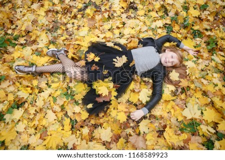 beauty, people, season and health concept - pretty little girl is lying in yellow Autumn leaves