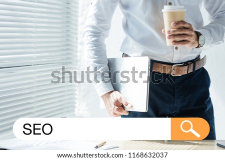 cropped view of developer holding laptop and coffee to go, with SEO search bar