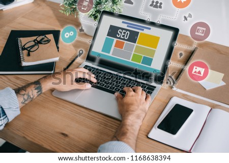 cropped shot of developer using laptop with SEO icons at workplace