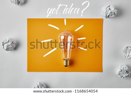 top view of incandescent lamp on blank yellow paper with "got idea?" lettering surrounded with crumpled papers on white surface
