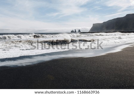 Waves crashing against black sand beach Vik in Iceland with cliffs and mountain in the background