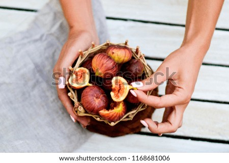 Ripe sweet figs in a basket with female hands isolated on white wooden background. Female hands break a ripe juicy fig