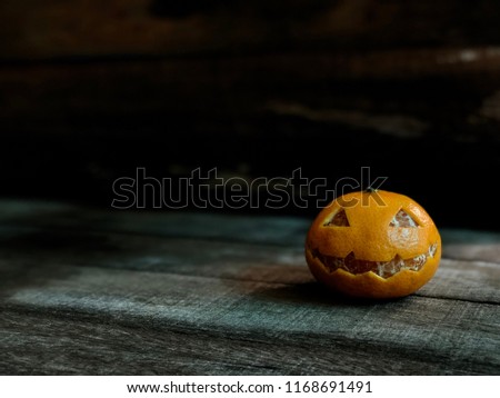 Fresh Orange with smiling face like the pumpkin for Halloween festival, on old wood, with dark tone, rural style. Decorative with carve fruits, with space for text.