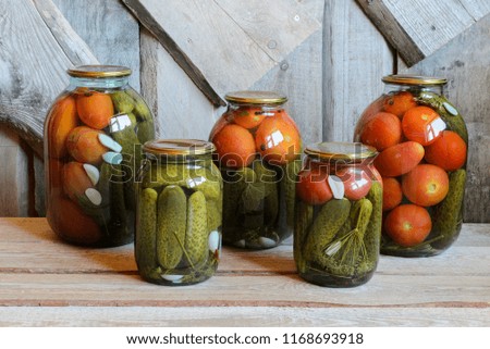 Glass jars with canned tomatoes and cucumbers. Wooden background