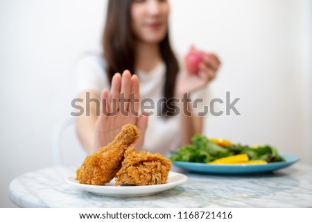 Dieting or good health concept. Young woman rejecting Junk food or unhealthy food such as fried chicken or dessert and choosing healthy food such as fresh fruit or vegetable. Royalty-Free Stock Photo #1168721416