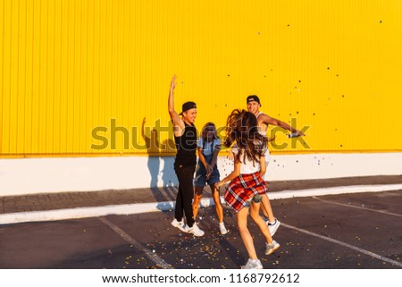 Beautiful cool young jump with confetti on a yellow background, a group of young people celebrating and having fun, summer mood, friends walking in the city in place, party in the Parking lot