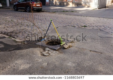 Vintage tragic conceptual picture of poor quarter of old city. Destroyed paving slab with asphalt remains. Hole of road well without an onion cover is fenced for safety by domestic mops