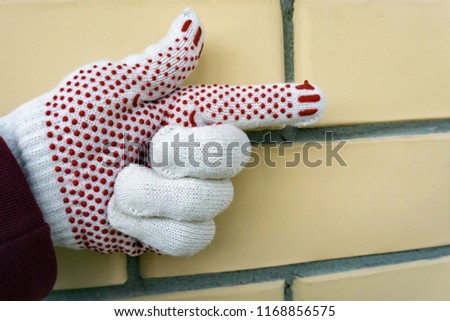 An indicative hand gesture. A hand in the construction glove points to the right against a yellow brick wall.