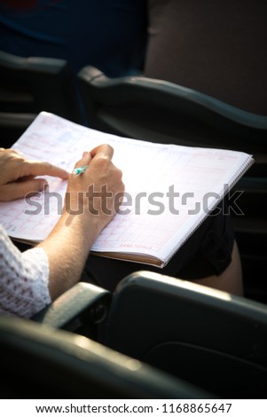 Baseball fan keeping score in a scorekeepers book, with space for text on top and bottom