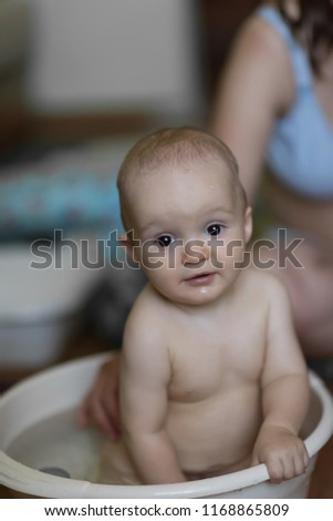 baby boy indoor bathing in the small white bathtub . He is smiling and full of happiness.