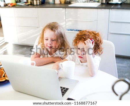 Brother and sister are sitting in the kitchen at the computer table watching cartoons