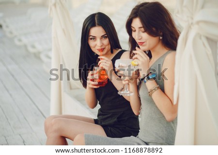 two beautiful young girls sitting at the summer pier and drinking cocktail