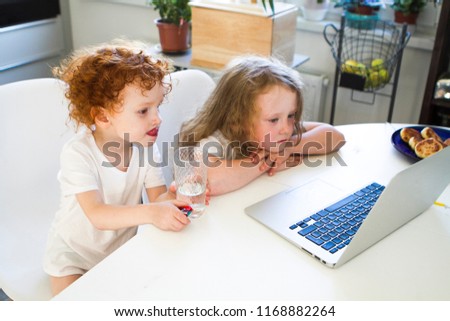 Brother and sister are watching a cartoon on a laptop. Children sit at the computer table