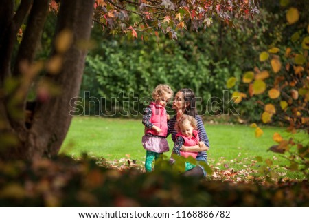 Mother and identical twins having fun in the park in autumn, blond cute curly girls, happy family, beautiful girls in pink jackets, young family in park in autumn, healthy lifestyle, autumn colorful 