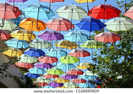 a lot of colored open umbrellas hang against the sky on the street