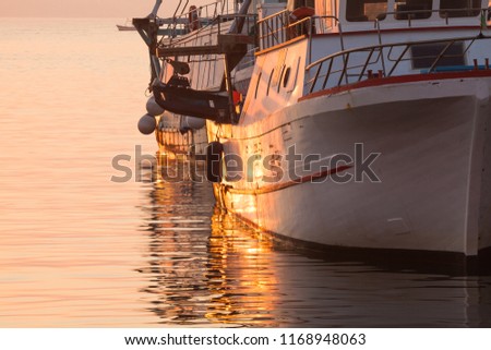 Some beautiful fishing boats are slowly rocking in harbor during a beautiful orange sunrise
