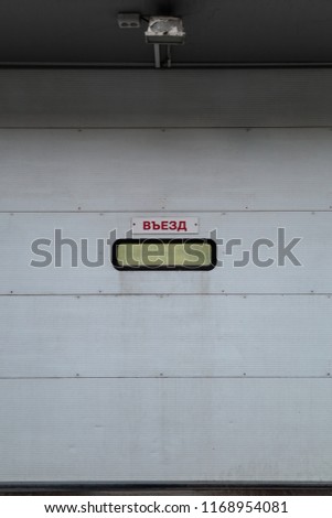 Entrance to the car wash in the car service. Lookout window on the gray roll up plastic door. Inscription on the plate in Russian "Entry"