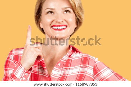 Beautiful woman smiling pointing up. Beautiful student girl showing finger up on yellow background
