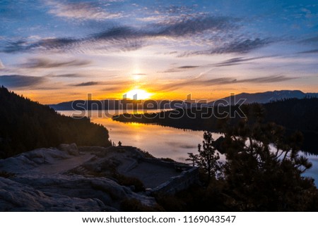 Sun crests over mountains behind emerald bay reflections Amazing Sunrise over Lake Tahoe , California majestic Sierra Nevada Mountain Lake Landscape tiny silhouette of person all alone