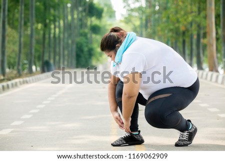 Picture of fat woman wearing sportswear and tying her shoelaces on the road