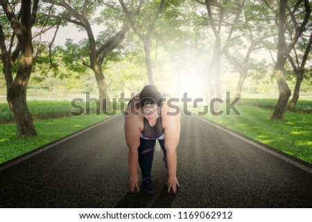 Picture of Asian fat woman ready to run while kneeling on the road. Shot with sunlight background