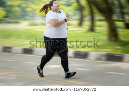 Picture of obese woman wearing sportswear while sprinting on the road with fast motion