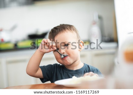 The little boy in the kitchen eagerly eating rice with a spoon independently