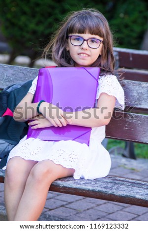 portrait of student with notebook and backpack sitting on park bench