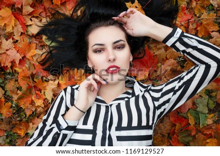 beauty, people, season and health concept - pretty girl is lying in yellow red Autumn leaves