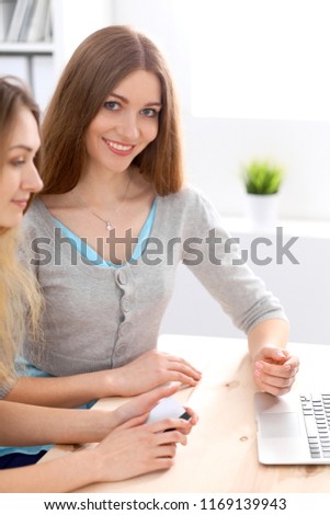 Two friends or sisters talking taking a conversation at the table with laptop