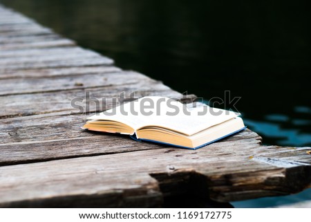 Open book on a wooden bridge above the river. Reading in the fresh air. Royalty-Free Stock Photo #1169172775