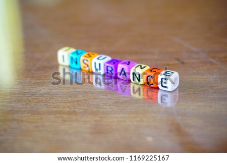 Conceptual of insurance in balance sheet item in financial accounts spelled on colorful alphabet beads. Isolated over reflective dark wooden surface. Focus on beads in foreground.