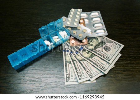Pillbox, pills and tablets on dollar money on dark wooden table. Medicine expenses. High costs of medication concept