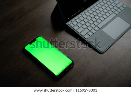 A Computer Tablet and ultra-slim smartphone with green screen/chroma key on brown table