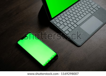 A Computer Tablet and ultra-slim smartphone with green screen/chroma key on brown table
