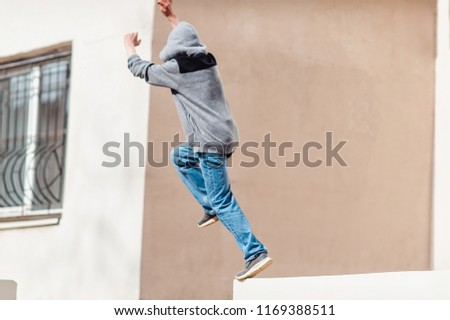 Teenage boy in the hood on a street in a big city next to a high-rise building alone. concept of a teenager parkour life. parkour jump portrait on the street in a big city