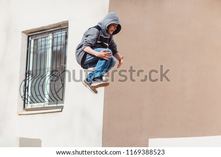 Teenage boy in the hood on a street in a big city next to a high-rise building alone. concept of a teenager parkour life. parkour jump portrait on the street in the big city close