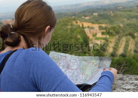 Girl studies tourist map on a medieval wall of European city. Italy, Montepulciano