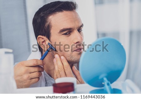 Man with razor. Dark-haired good-looking man holding razor in his hand whie shaving his face in the bathroom