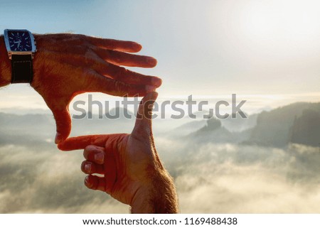 Fingers gesturing picture frame on sunrise.  Fingers making frame. Orange misty valley bellow. Sunny spring daybreak in mountains