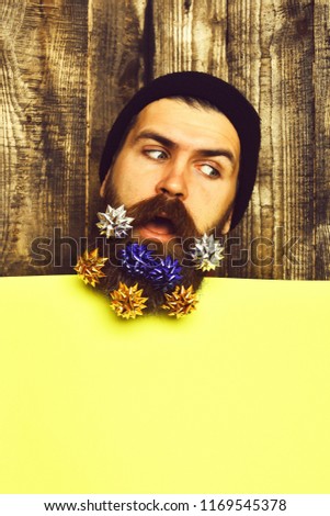 Bearded man, long beard. Brutal caucasian thoughtful hipster with colorful gift decoration stars in moustache, yellow paper sheet on brown wooden vintage studio background