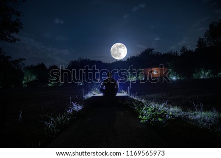Silhouette of man in the forest on the night. Silhouette of person standing in the dark forest with light. Dark night in forest. Surreal night forest scene. Horror Halloween concept.
