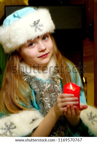 A nice little girl in a New Year's suit is holding a candle. The concept of a Christmas family holiday, children's emotions.