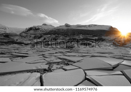 Winter Sun rise peaking over Glacier in Iceland.  Photo Black and white except for the sun. 