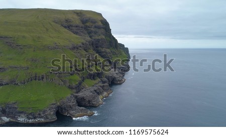 AERIAL, COPY SPACE: Flying towards a breathtaking cliff and empty grasslands overlooking the endless cold ocean. Picturesque shot of rugged Scandinavian coastal nature on a cloudy day in Faroe Islands