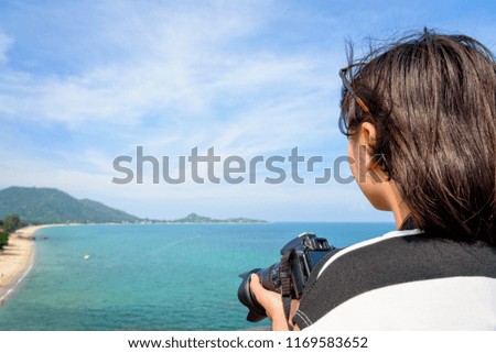 Teenage girl is holding a dslr camera on high and beautiful nature landscape of the blue sea on Lamai beach hight viewpoint during summer travel at Koh Samui island, Surat Thani, Thailand